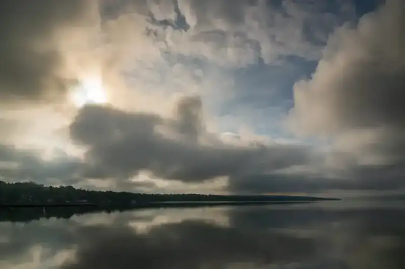 Clouds breaking over the still water of a Finger Lake, with the far shore in silhouette