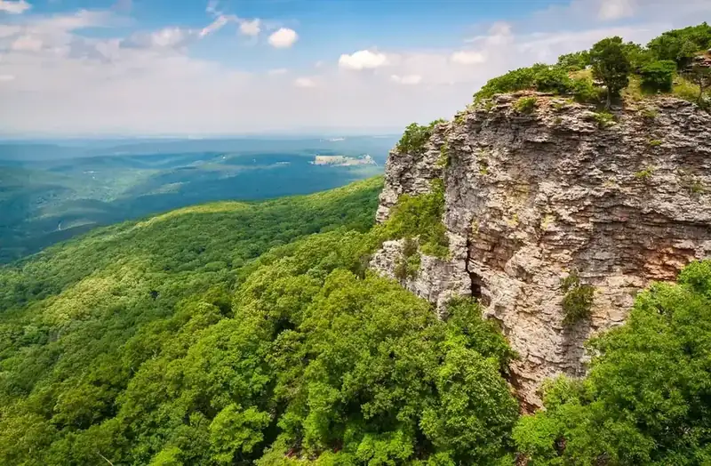 A limestone cliff dropping away above forested ridges in the Ouachita Mountains