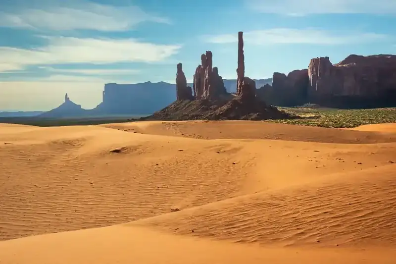 The Totem Pole and its neighboring spires rising above rippled sand dunes in Monument Valley