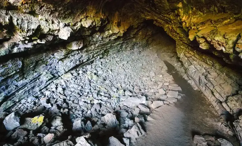 The rubble floor and low ceiling of a lava tube cave, lit from the entrance