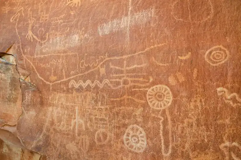 A panel of petroglyphs pecked into a red sandstone wall